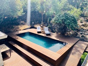 A pool with wooden deck and chairs in the middle of it