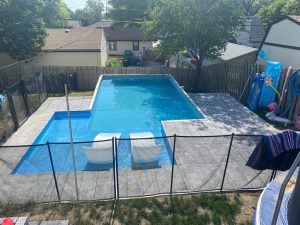 A pool with a fence around it and chairs in the middle of the yard.