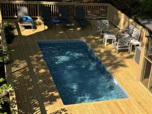 A pool with a deck and chairs in the background.